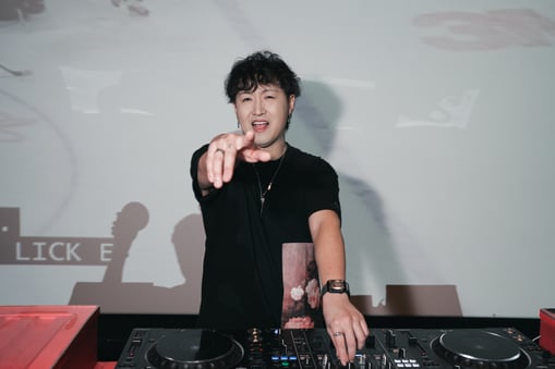 A producer and DJ pointing into the camera behind a DJ deck.